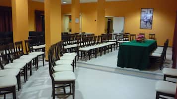 Une salle de conférence avec des rangées de chaises en bois et une table recouverte d’une nappe verte.