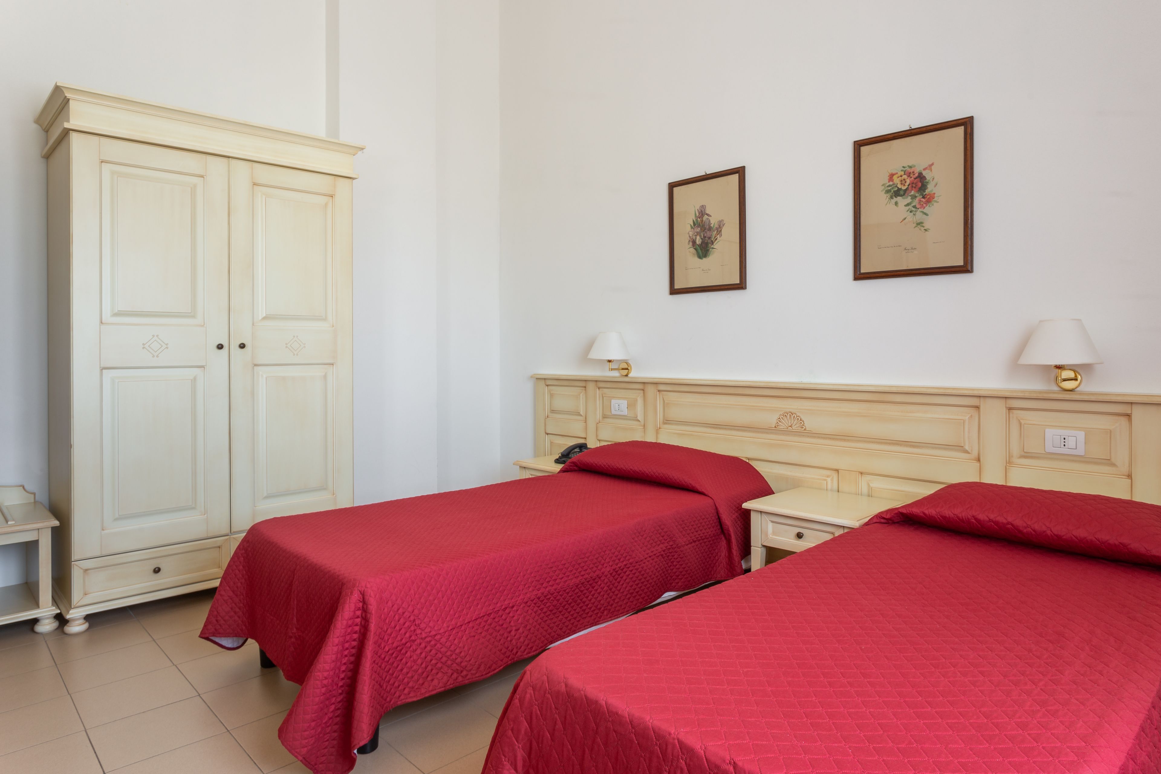 A room with two single beds, a wardrobe, and two wall-mounted lamps.