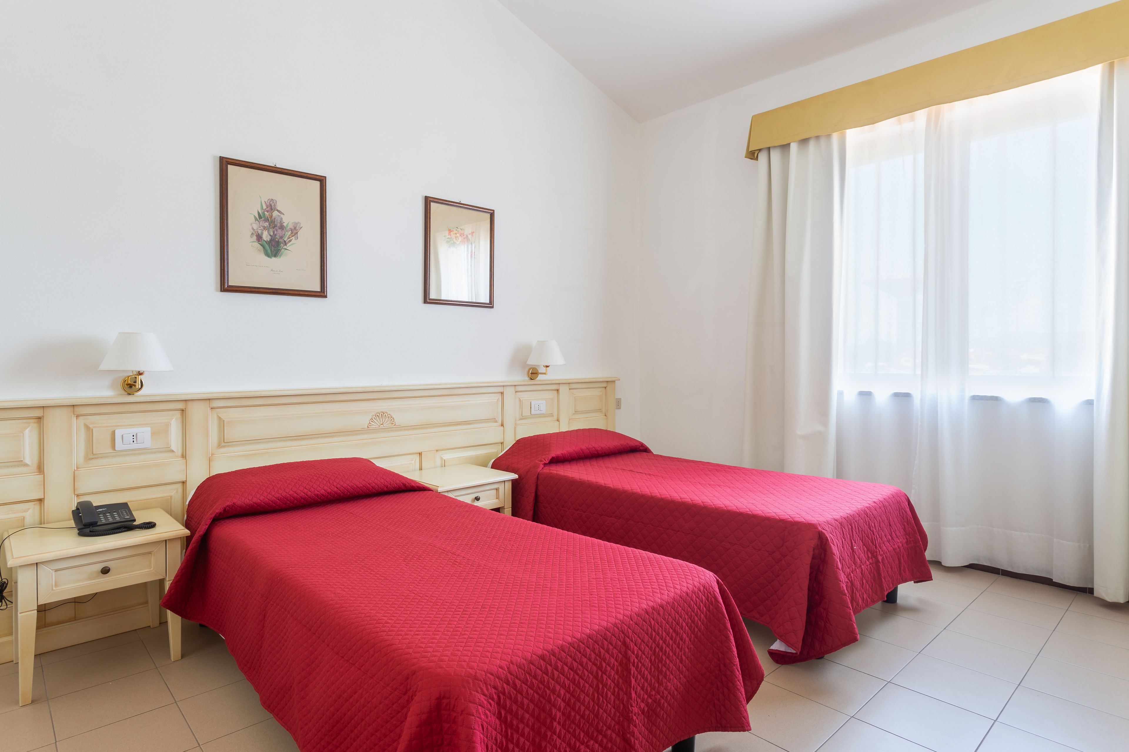 A hotel room with two single beds, a bedside table with a lamp, a phone, and a framed picture on the wall.