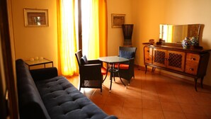 Una sala de estar con un sofá, una mesa, sillas, un armario y una ventana con cortinas.