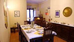 Comedor con mesa lista para cuatro, sillas, un jarrón con flores y una cocina al fondo.