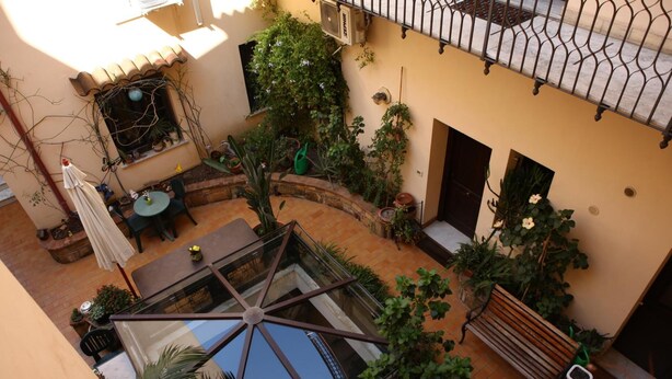 Un patio con una mesa de vidrio, sillas, un banco y plantas en macetas.