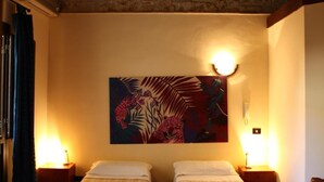 Una habitación con dos camas individuales, una pared de piedra, un cuadro y dos lámparas de noche.