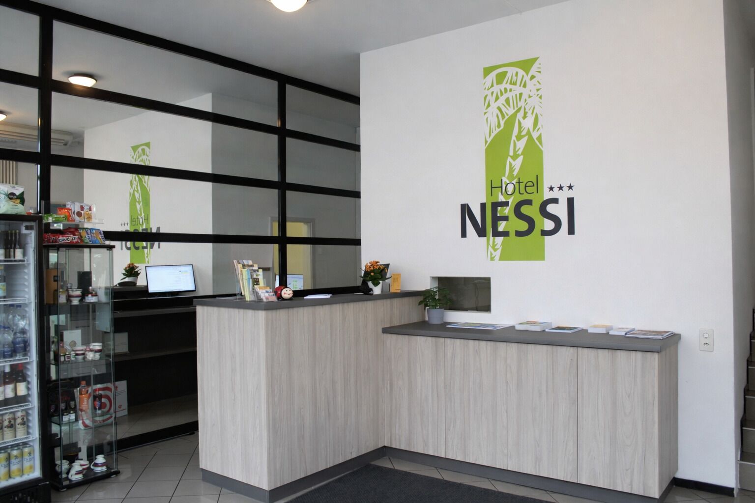 Una recepción de hotel con diseño moderno, un expositor de vidrio con servicios y un cartel en la pared para Hotel NESSI.