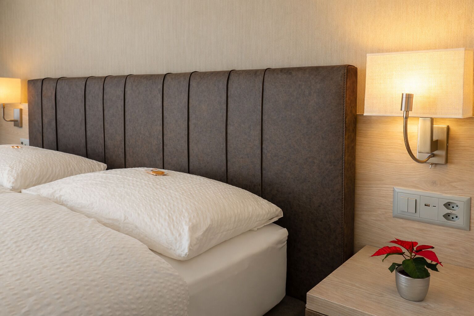 Une chambre d’hôtel avec un grand lit, une table de chevet avec une lampe et une prise électrique au mur.