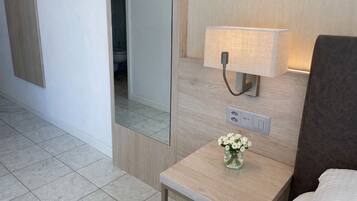 A hotel room with a bedside table, a lamp, a mirror, and a vase with flowers.