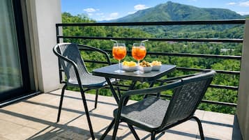 A balcony with two chairs and a table, two glasses of orange drink, and a bowl of snacks.