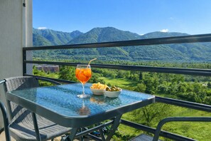 A balcony with a table set for a meal, a drink, and a view of mountains. - Hotel Nessi Locarno (Locarno)