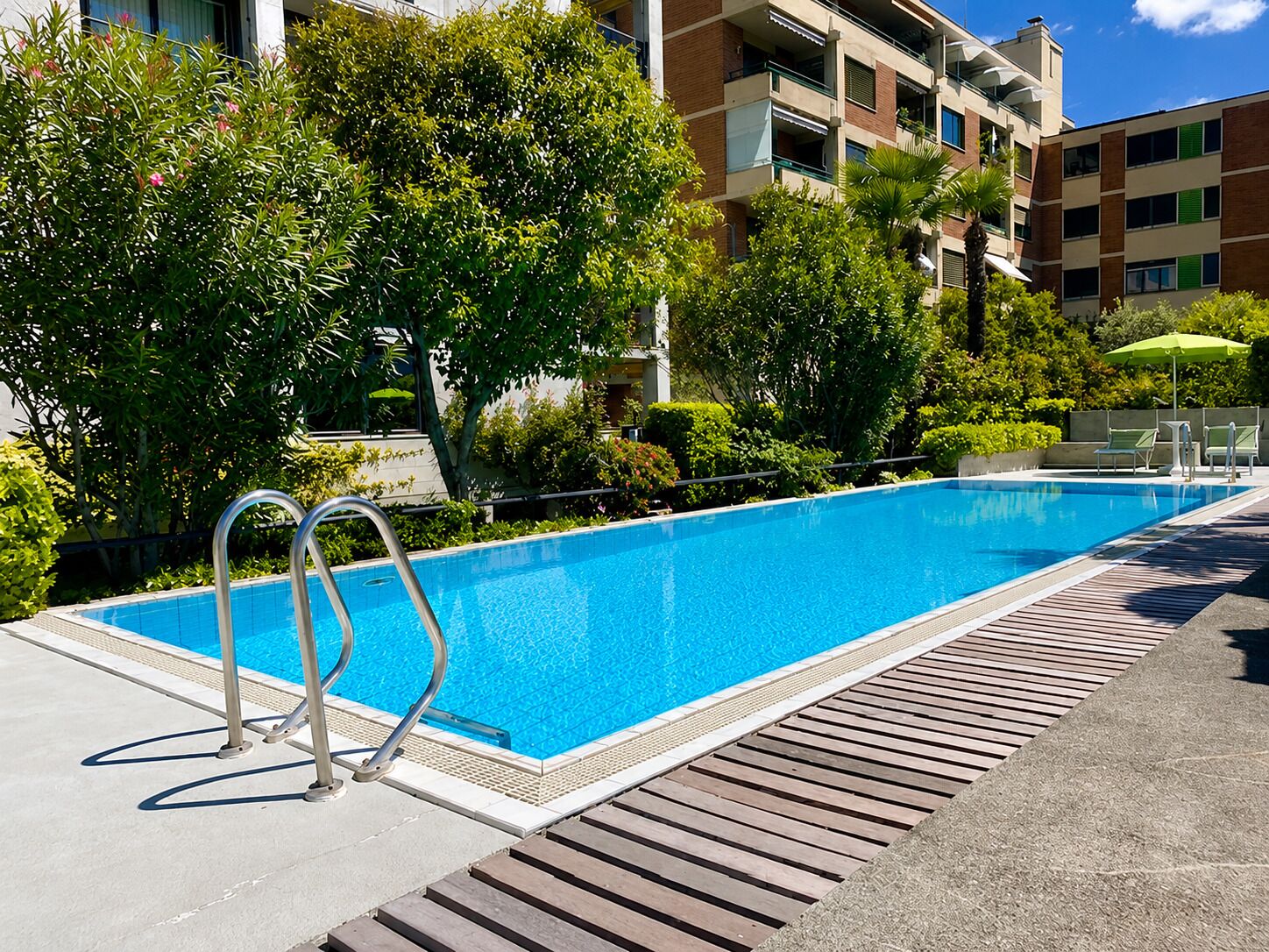 A rectangular swimming pool with a metal ladder, surrounded by greenery and a wooden deck.