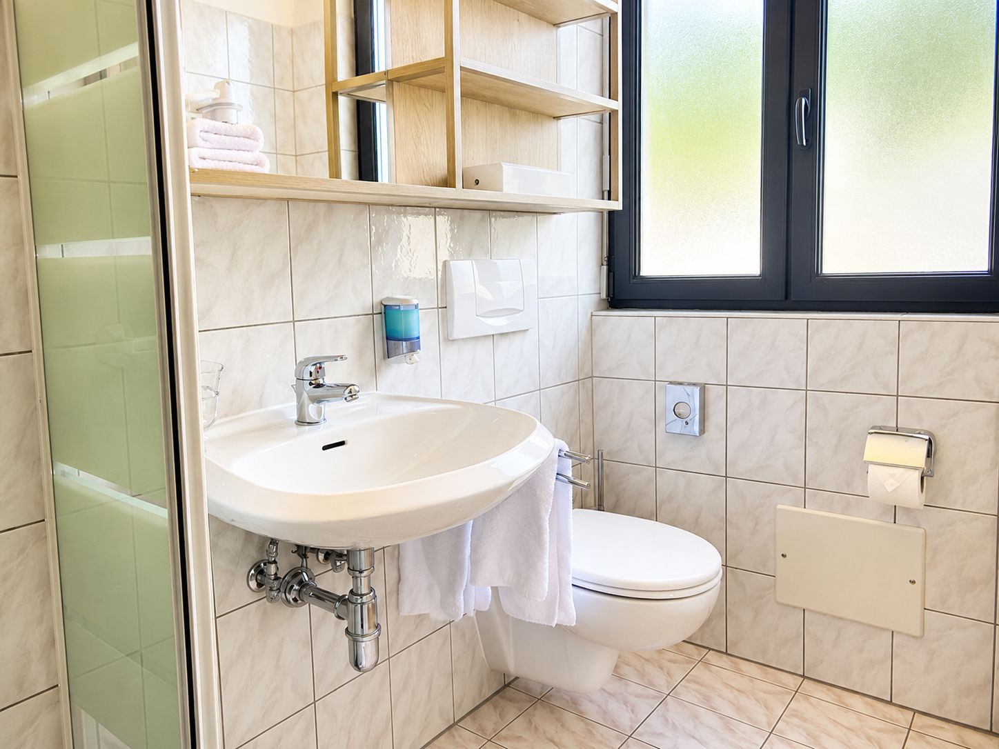 A bathroom with a white sink, a toilet, a glass shower enclosure, and a window with frosted glass.