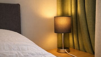 Een bed met een witte dekbedovertrek en een nachtkastje met een lamp en een stroomkabel.