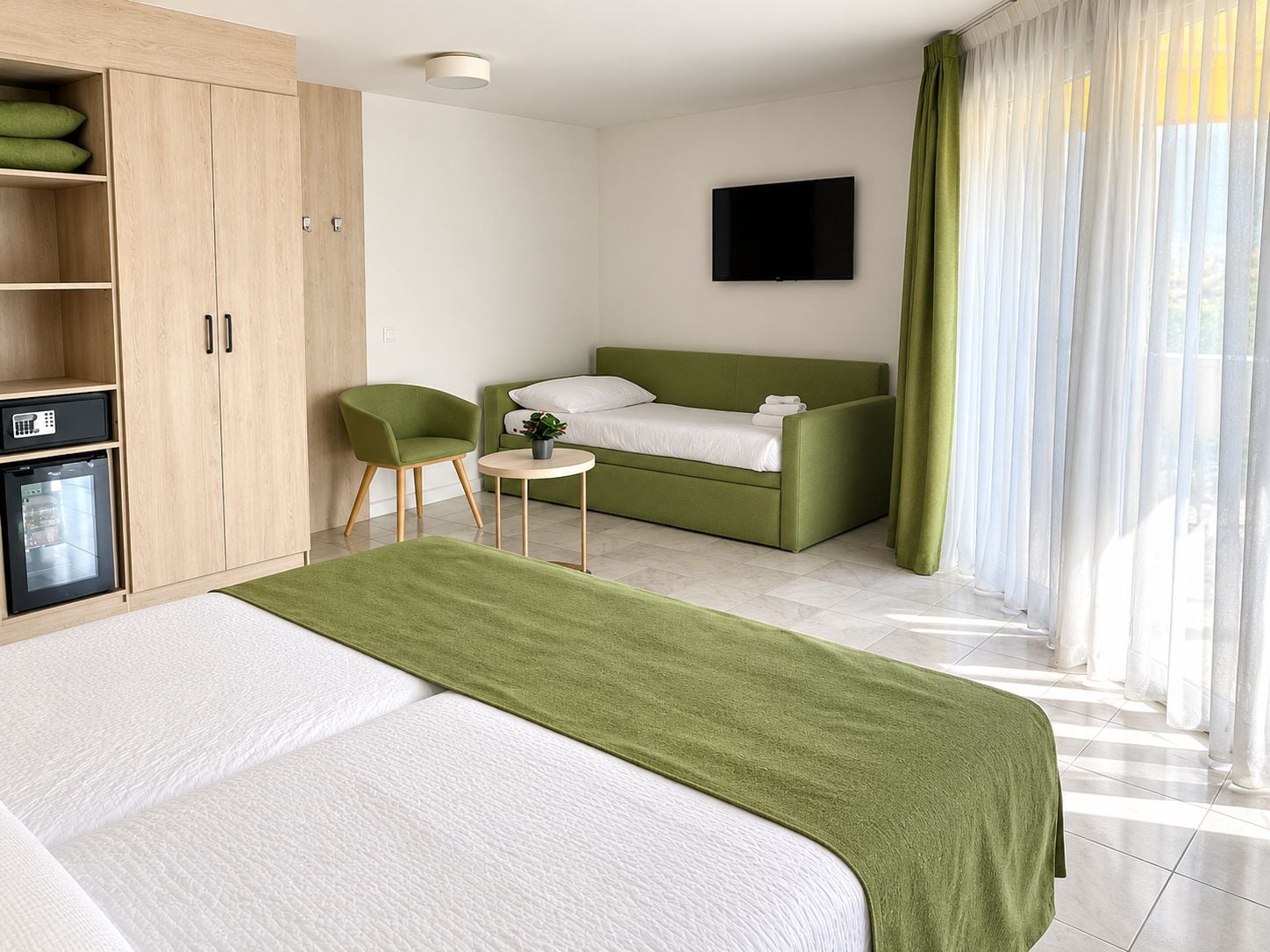 Habitación de hotel con cama, sofá verde, una mesita, una silla, televisor y un mini bar.