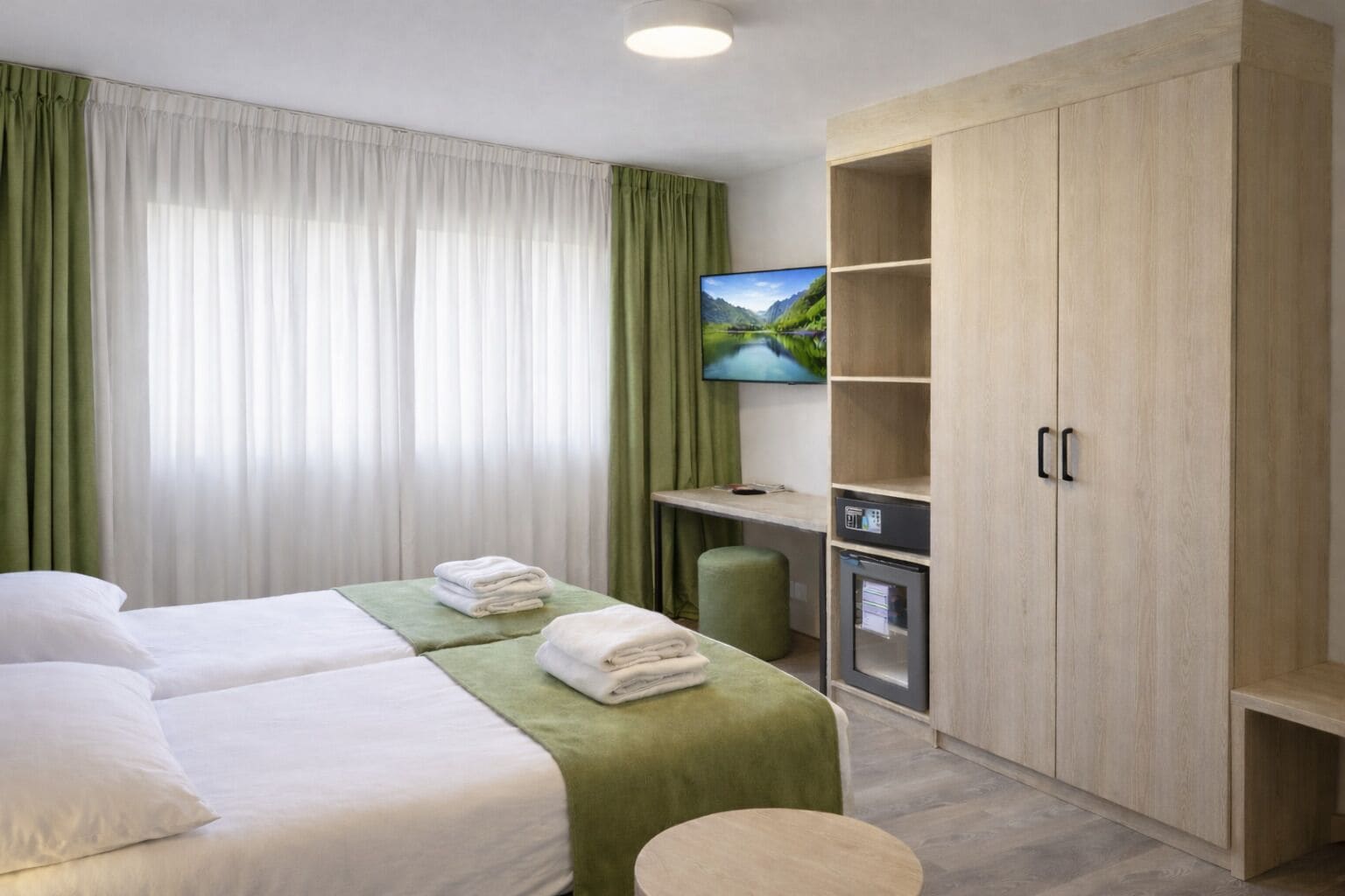 Habitación de hotel con dos camas, televisión, minibar y armario.