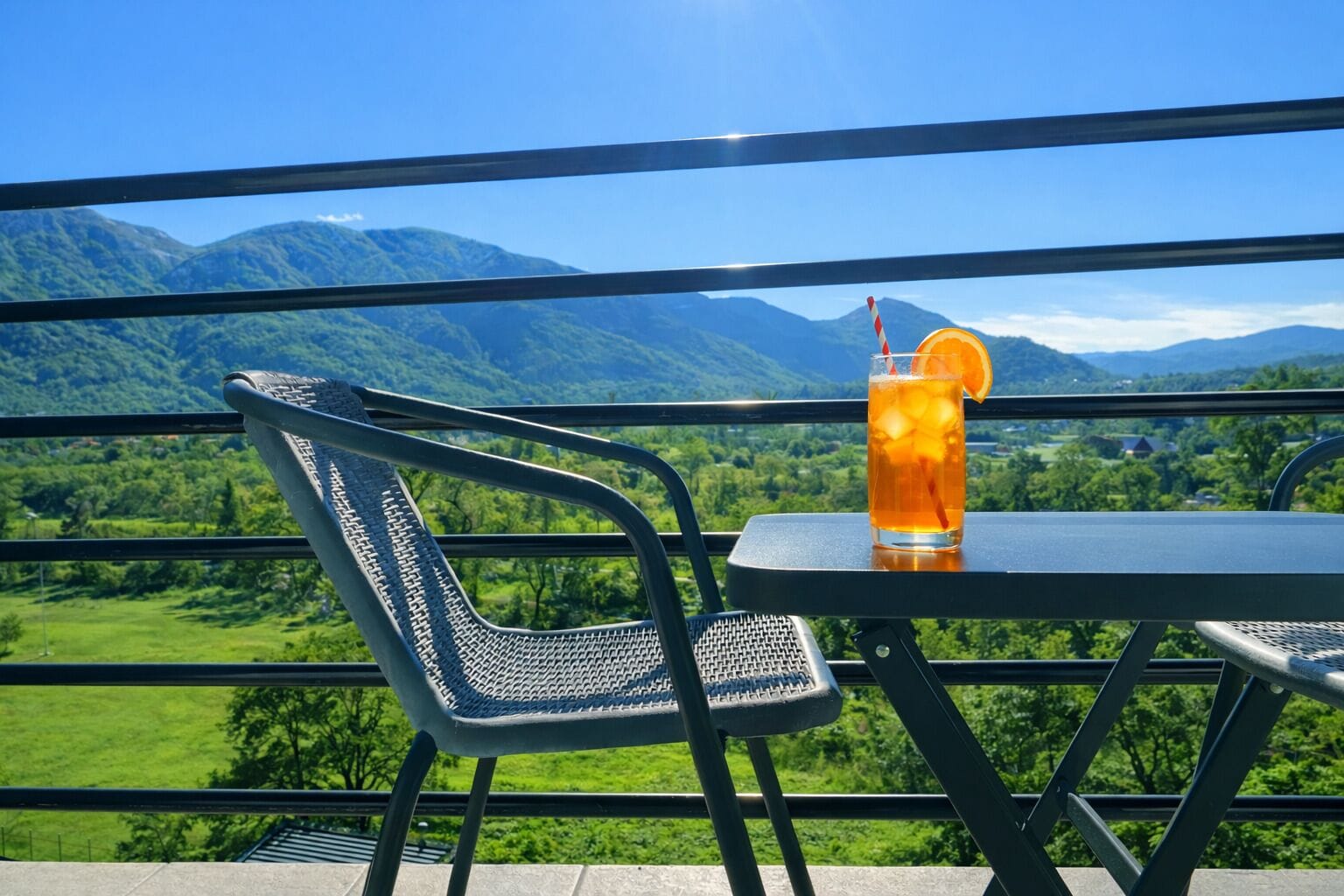 Una mesa con una bebida y una silla, con vista a un paisaje montañoso.