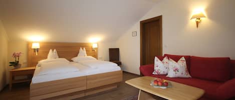 A bedroom with a wooden bed, a red sofa, and a small table with fruit.