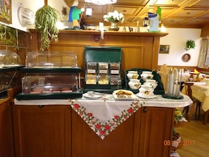 A buffet counter with various food items, a green sign with labels, and a floral table runner. - Schernthaner (St. Gilgen)