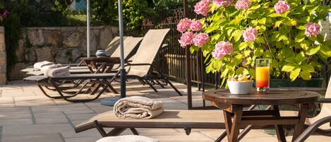 An outdoor seating area with lounge chairs, a table with a drink, and a flower arrangement.