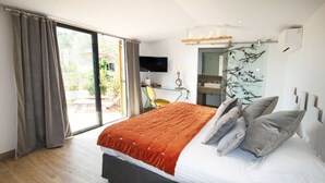 A bedroom with a large bed, a TV, a desk, and a sliding glass door to the outside. - Hotel du Clos (Le Rouret)