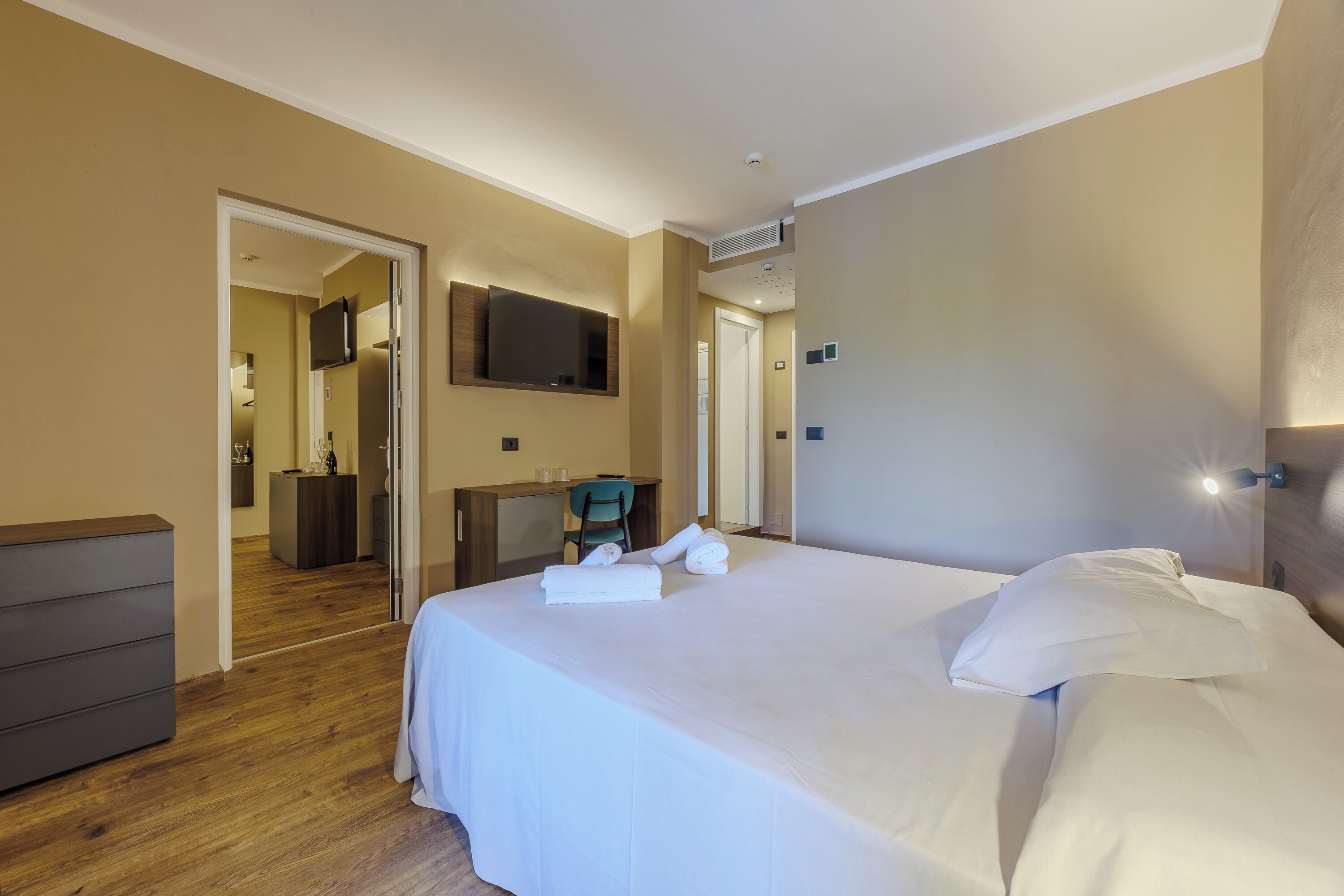 A hotel room with a large bed, a desk, a chair, and a television on the wall.