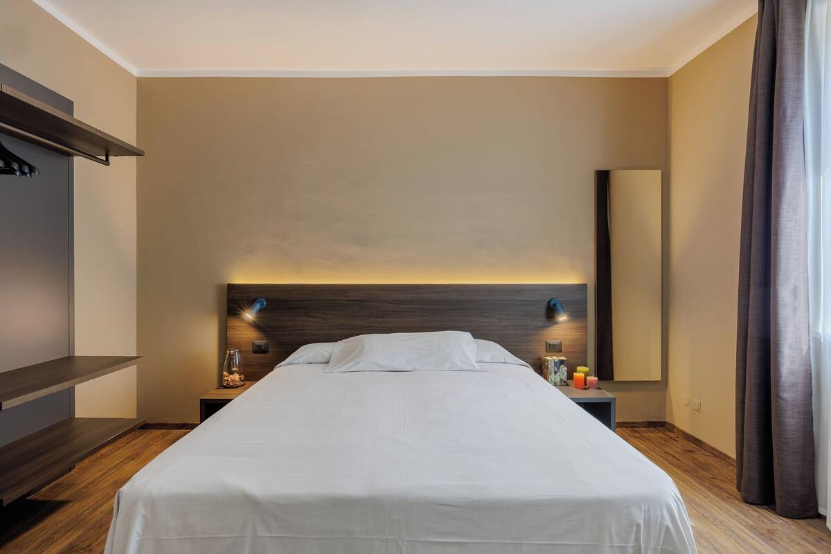 A hotel room with a large bed, bedside tables, a wardrobe, and a mirror.