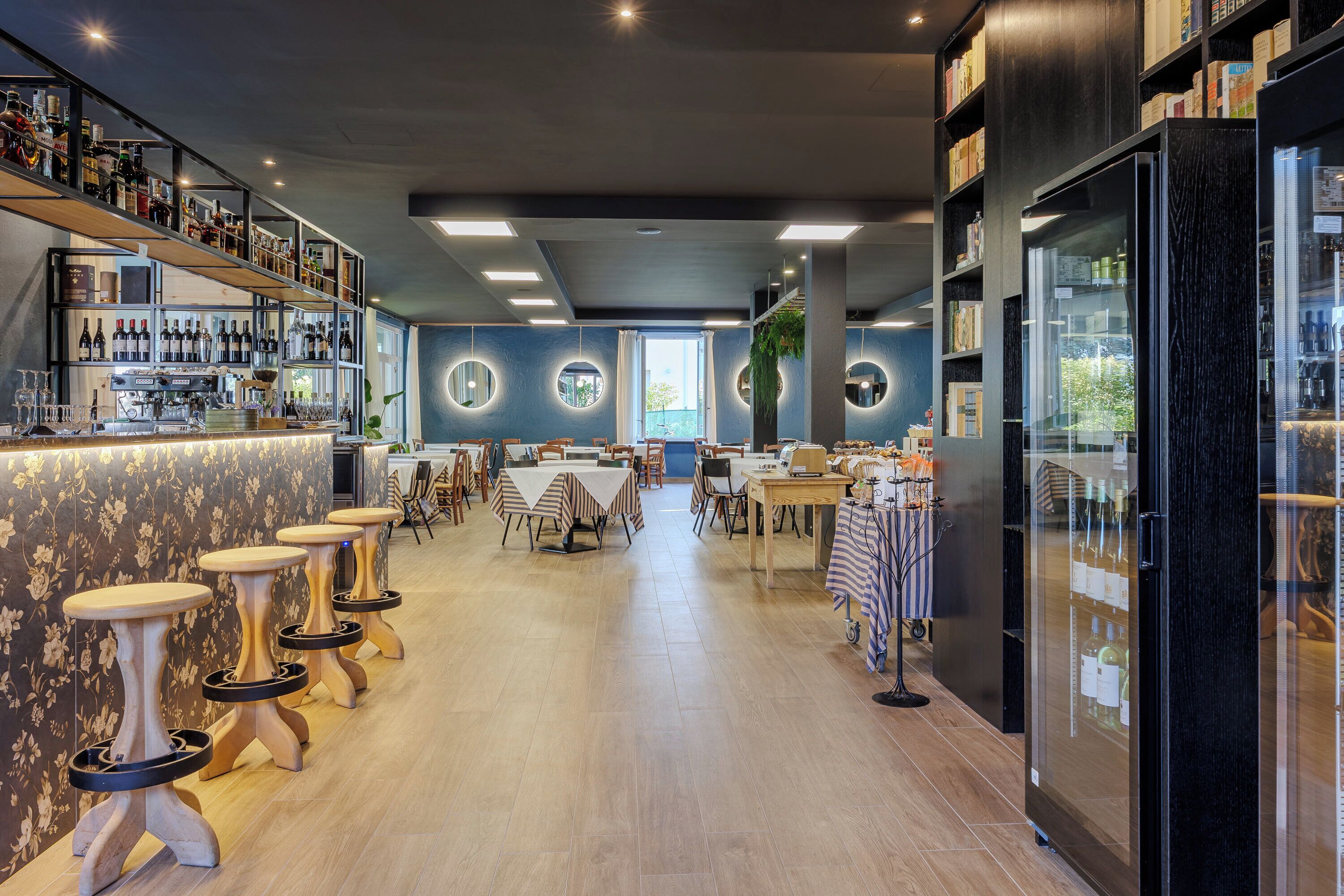 Un área de bar moderna con varias mesas y taburetes, una barra con botellas y un refrigerador grande.