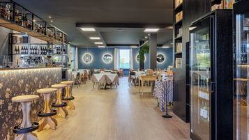 Un área de bar moderna con varias mesas y taburetes, una barra con botellas y un refrigerador grande.