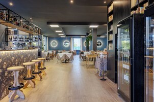 Un'area bar moderna con diversi tavoli e sgabelli, un bancone bar con bottiglie e un grande frigorifero.