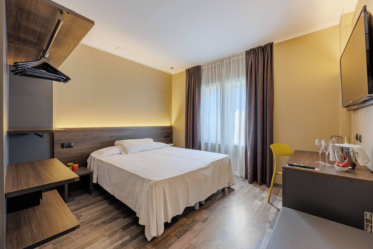 A hotel room with a bed, a desk, a chair, and a TV.