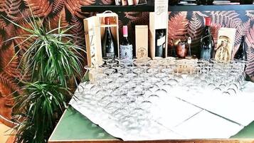 A wooden desk with multiple wine glasses and bottles, surrounded by potted plants and a fern-patterned backdrop.