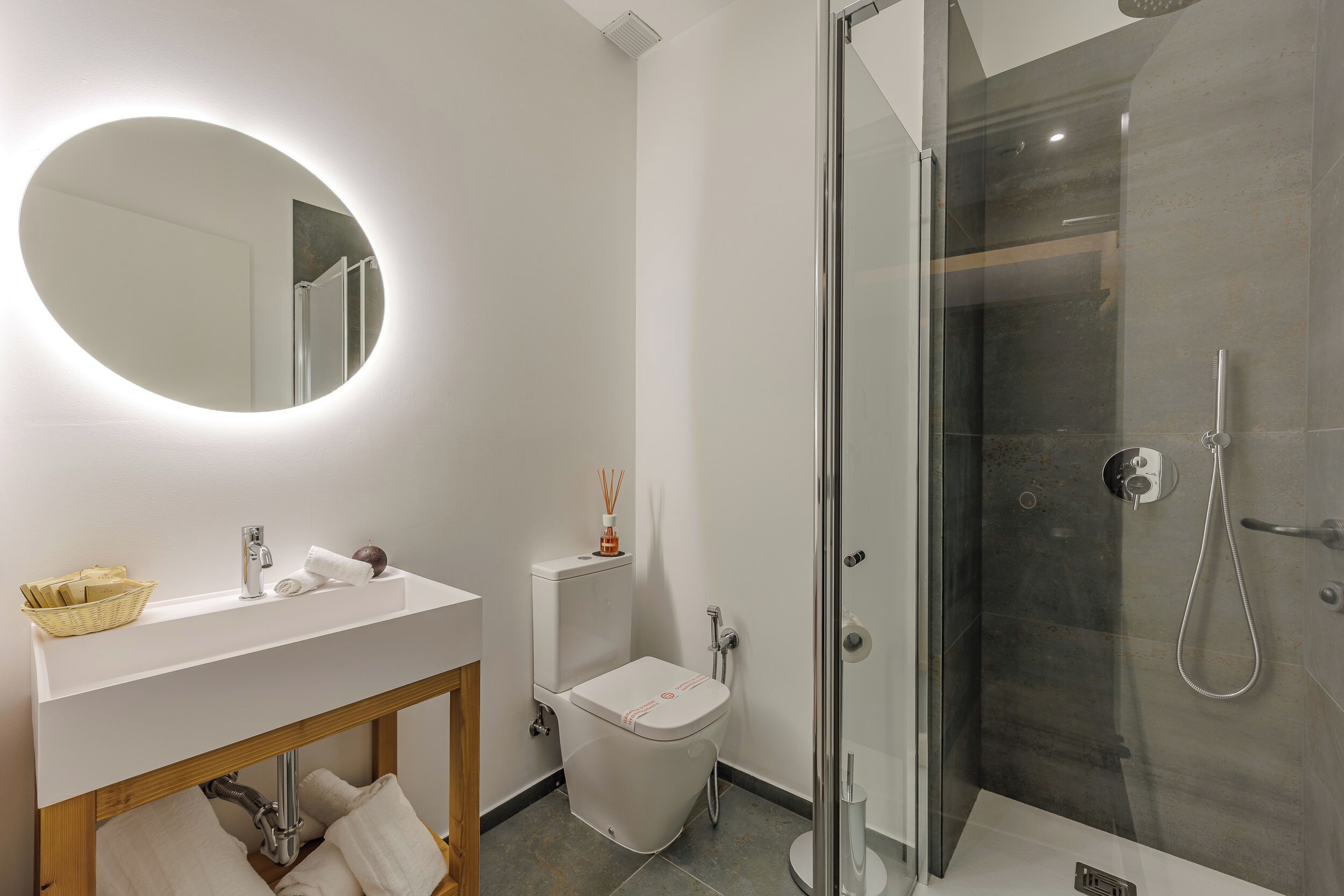 Une salle de bain moderne avec un meuble-lavabo blanc, un miroir rond, des toilettes et une douche à parois de verre.