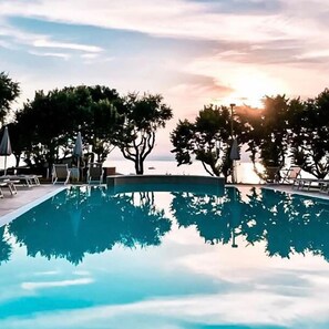 A swimming pool with lounge chairs and umbrellas, surrounded by trees, during sunset. - San Marco (Bardolino)