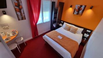 Une chambre d’hôtel avec un lit, un bureau, une chaise et des œuvres d’art accrochées aux murs.