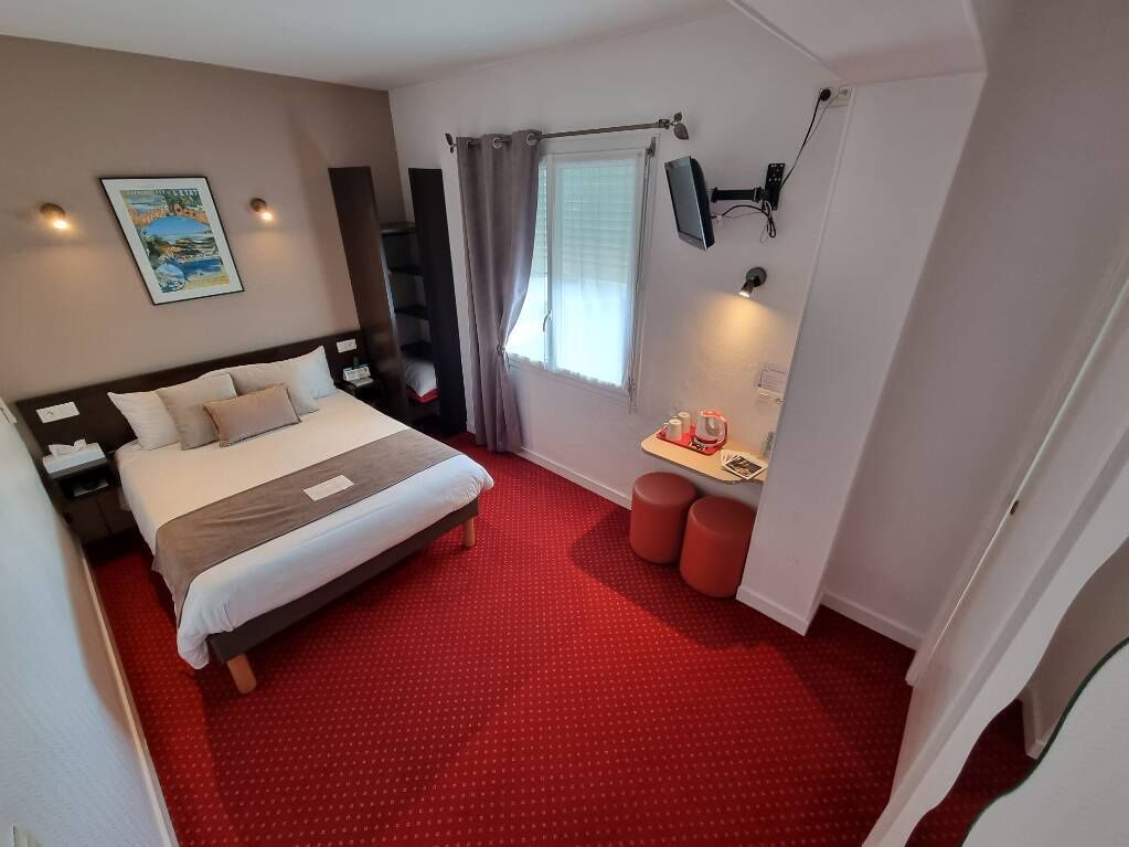 A hotel room with a large bed, a desk with a chair, a window with curtains, and a wall-mounted TV.