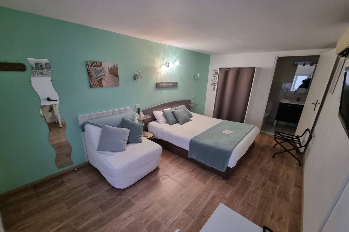 Habitación de hotel con dos camas, un sofá, una mesita y un televisor.