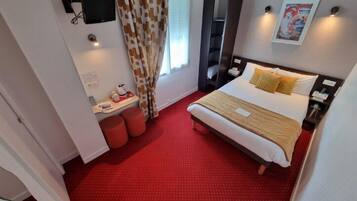 Una habitación de hotel con una cama, un escritorio con una silla, un televisor y una ventana con cortinas.
