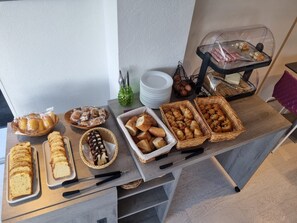 Una mesa de buffet con panes, pasteles y un expositor de vidrio con productos envasados.