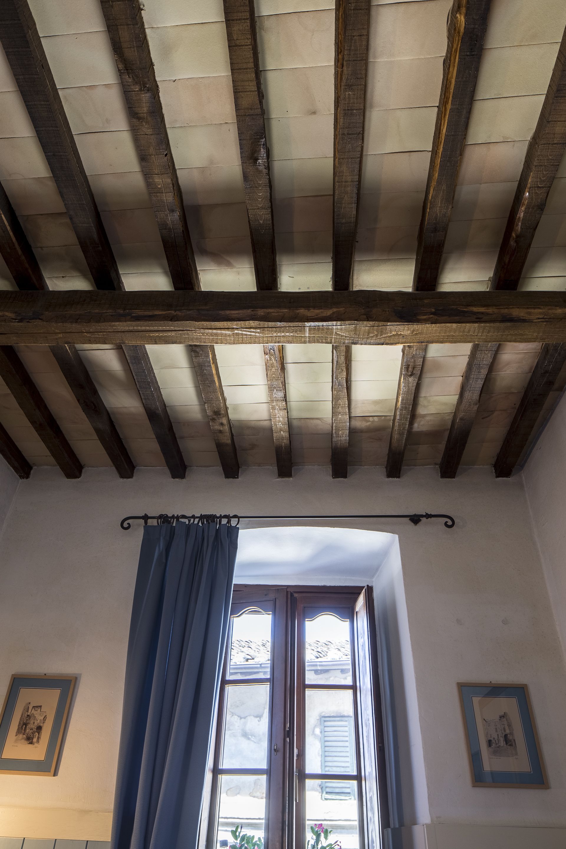 Ein Zimmer mit Holzboden, einem Fenster mit blauen Vorhängen und gerahmten Bildern an den Wänden.