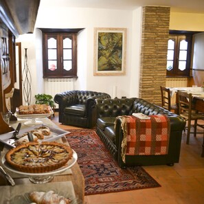 A living room with a leather sofa, a dining table with chairs, a large painting on the wall, and a buffet table with food. - Hotel Porta del Tempo (Stroncone)