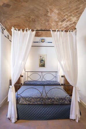 A bed with a metal frame and a quilted mattress, draped with white curtains. - Hotel Porta del Tempo (Stroncone)