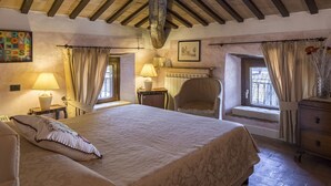 Quarto aconchegante com uma cama grande, uma cadeira, cômoda e janela com cortinas.