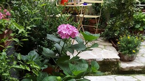 Área externa com piso de pedra, plantas em vasos e uma pequena mesa com cadeiras.