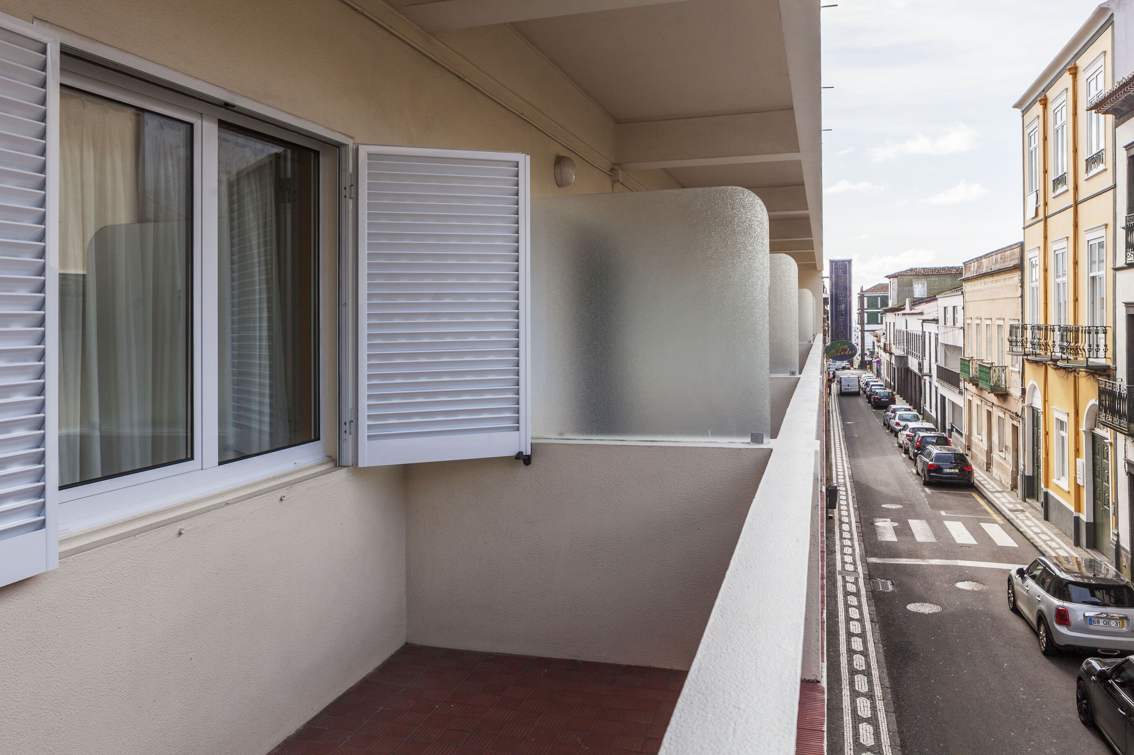 Ein schmaler Balkon mit Blick auf eine Straße, gesäumt von parkenden Autos und Gebäuden.
