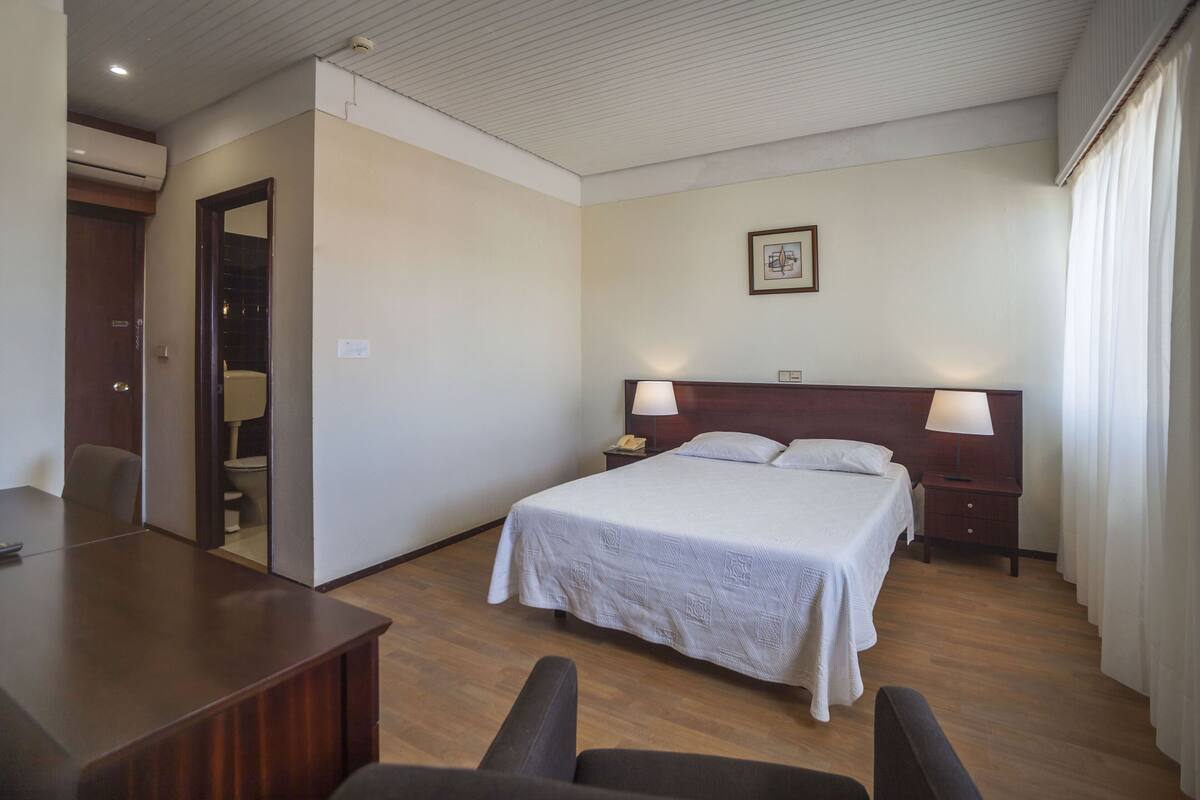 A hotel room with a large bed, bedside tables with lamps, a desk, and a chair.