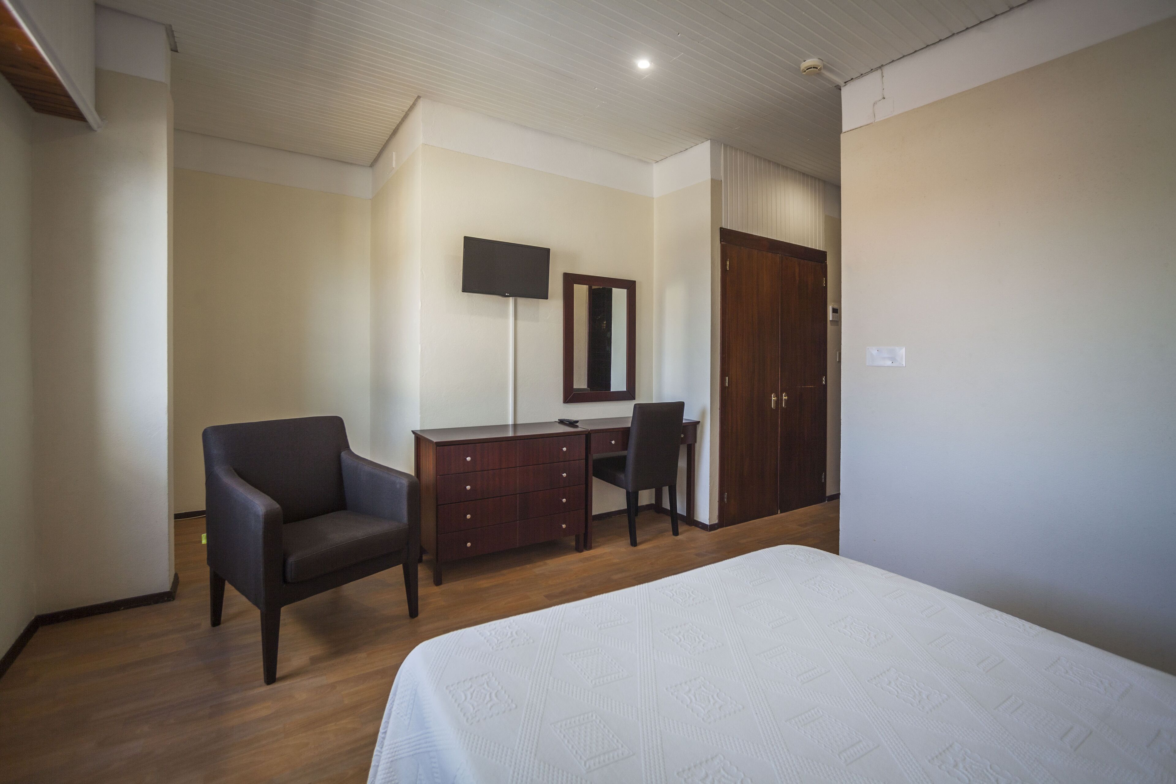 Ein Schlafzimmer mit Bett, Schreibtisch, Stuhl, Fernseher und Kleiderschrank.