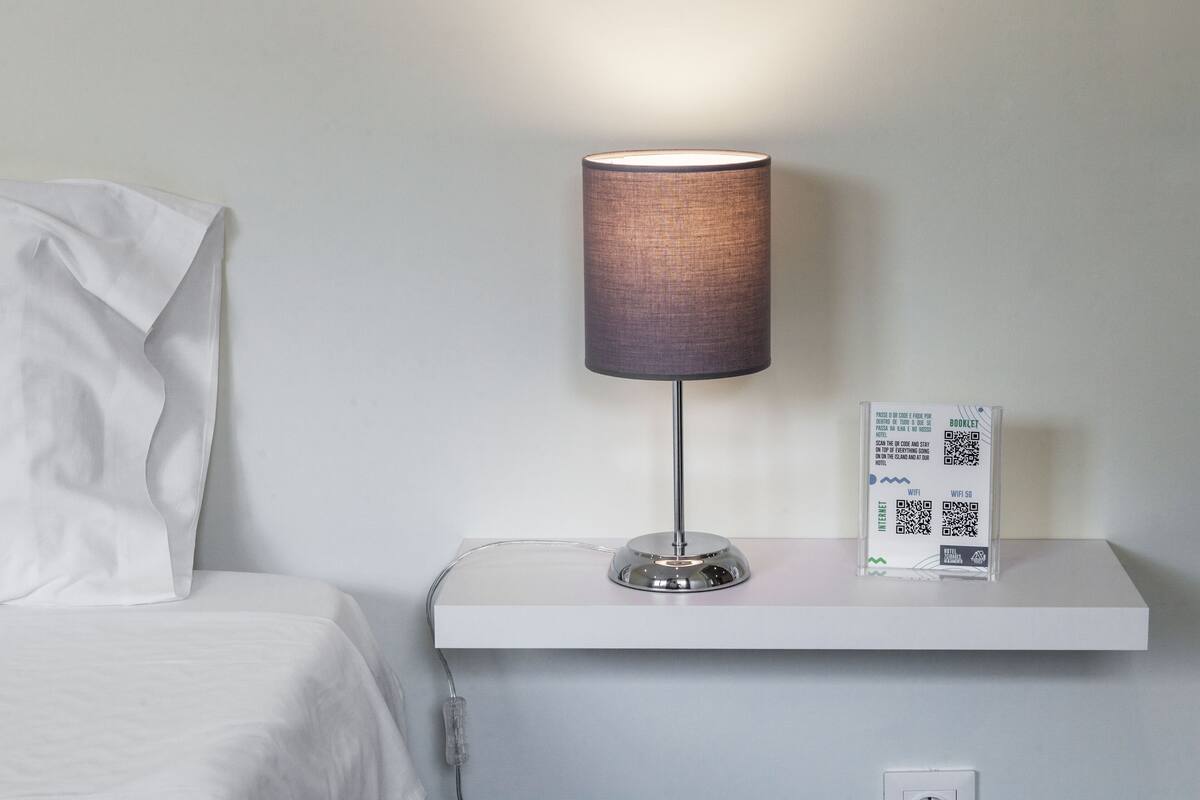A modern lamp with a cylindrical shade on a bedside table next to a bed.
