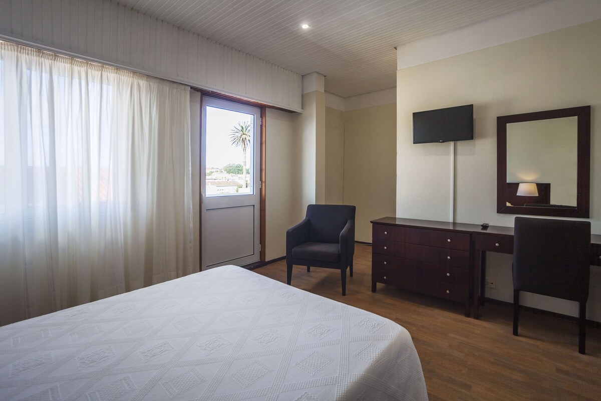 A hotel room with a bed, a desk, a chair, a television, and a window with curtains.