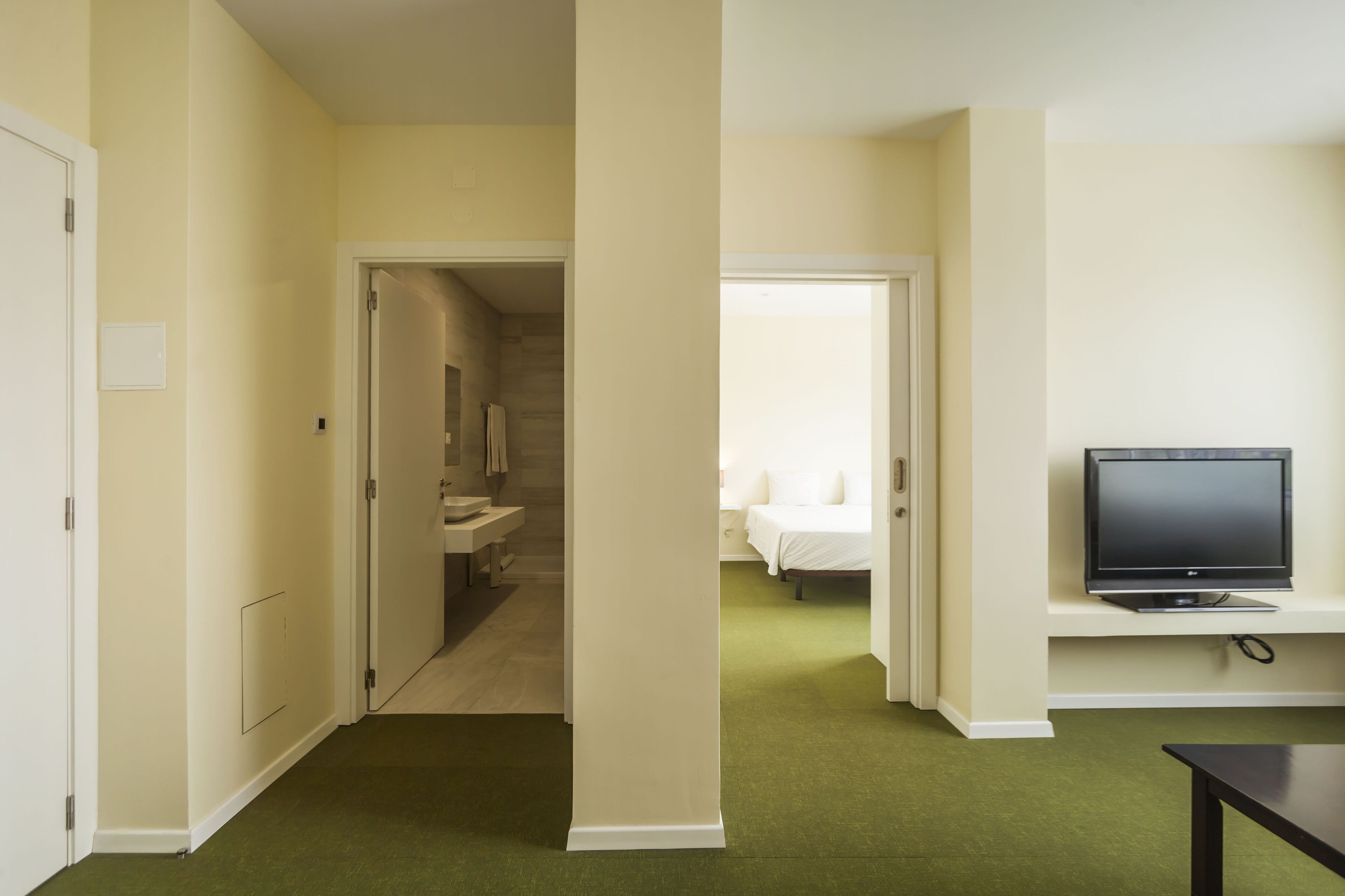 A hotel room with a bed, a television, and a bathroom visible through an open door.