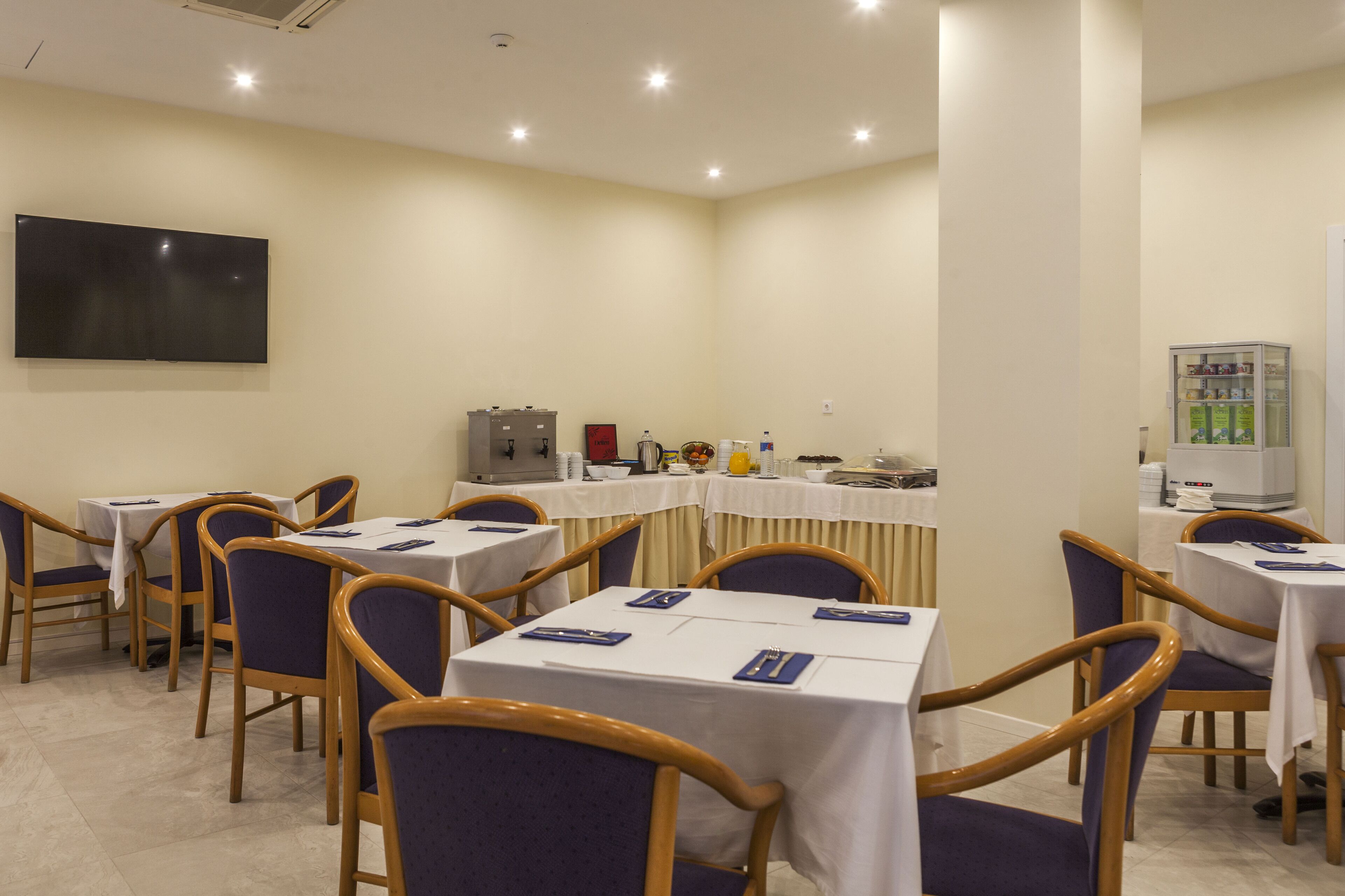 A conference room with tables and chairs, a flat-screen TV, and a refrigerator.