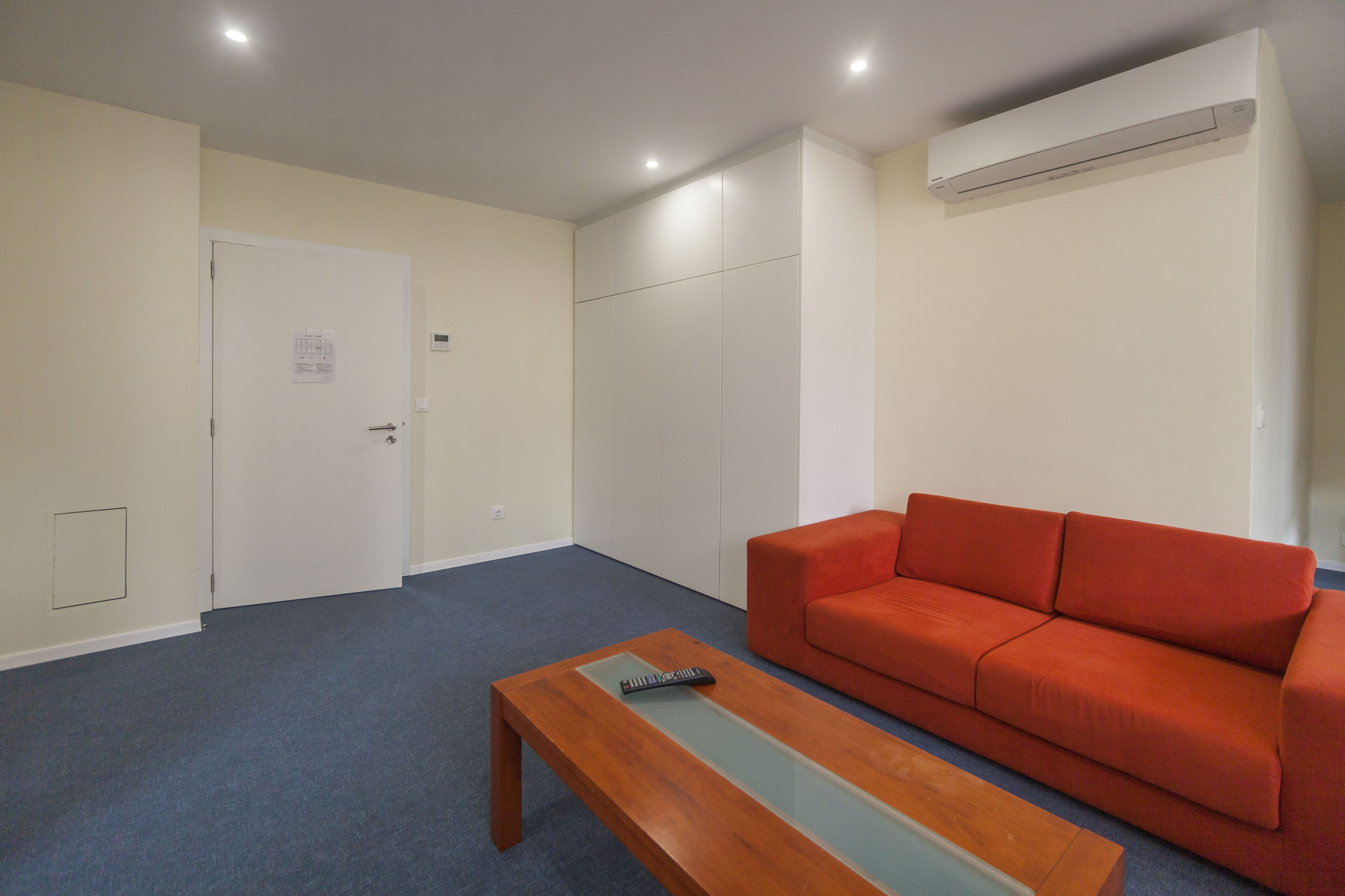 A room with a red sofa, a wooden coffee table, and a white door with a notice.