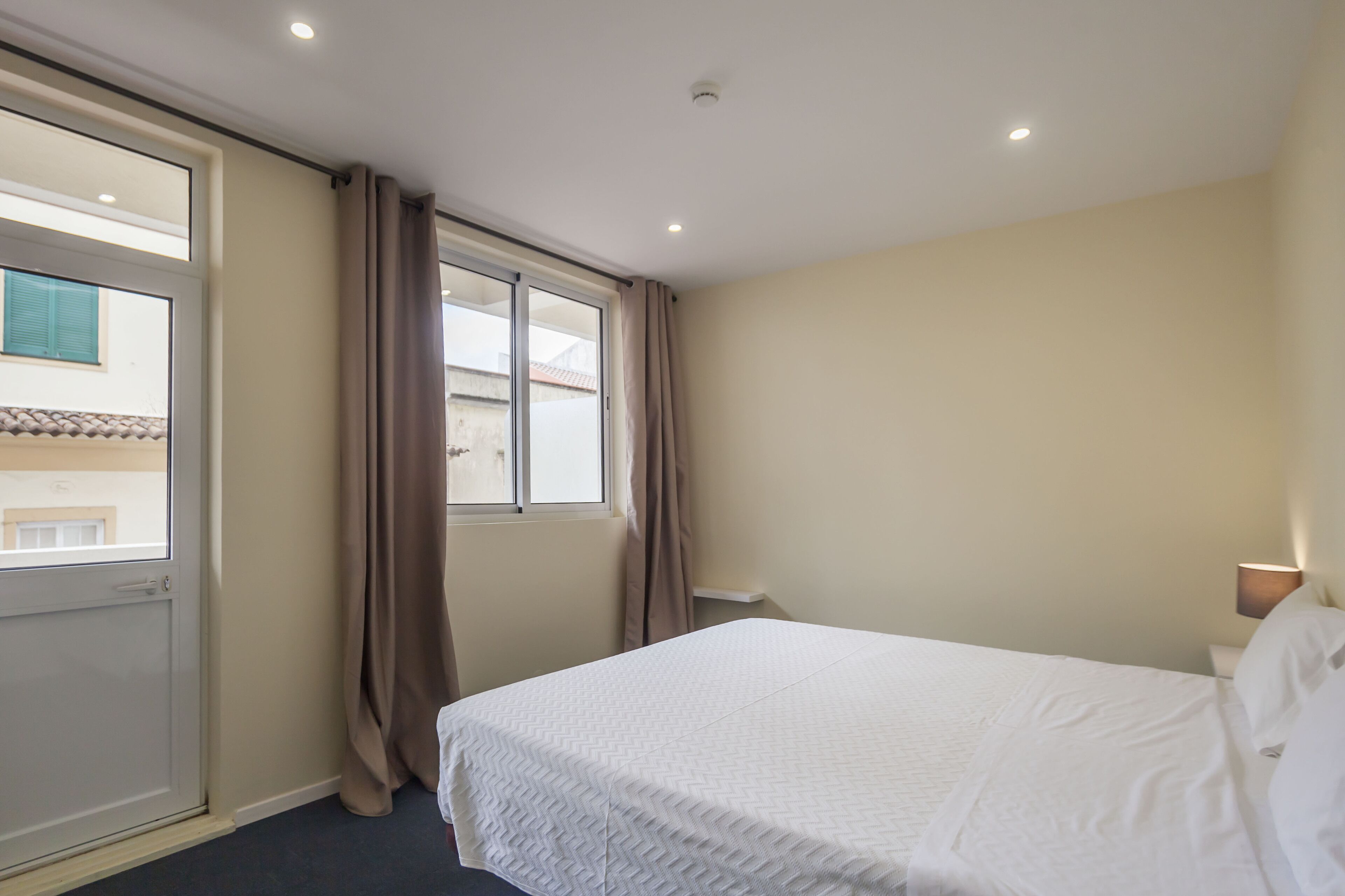 Une chambre d’hôtel avec un lit, une fenêtre avec des rideaux, une porte et un luminaire au plafond.